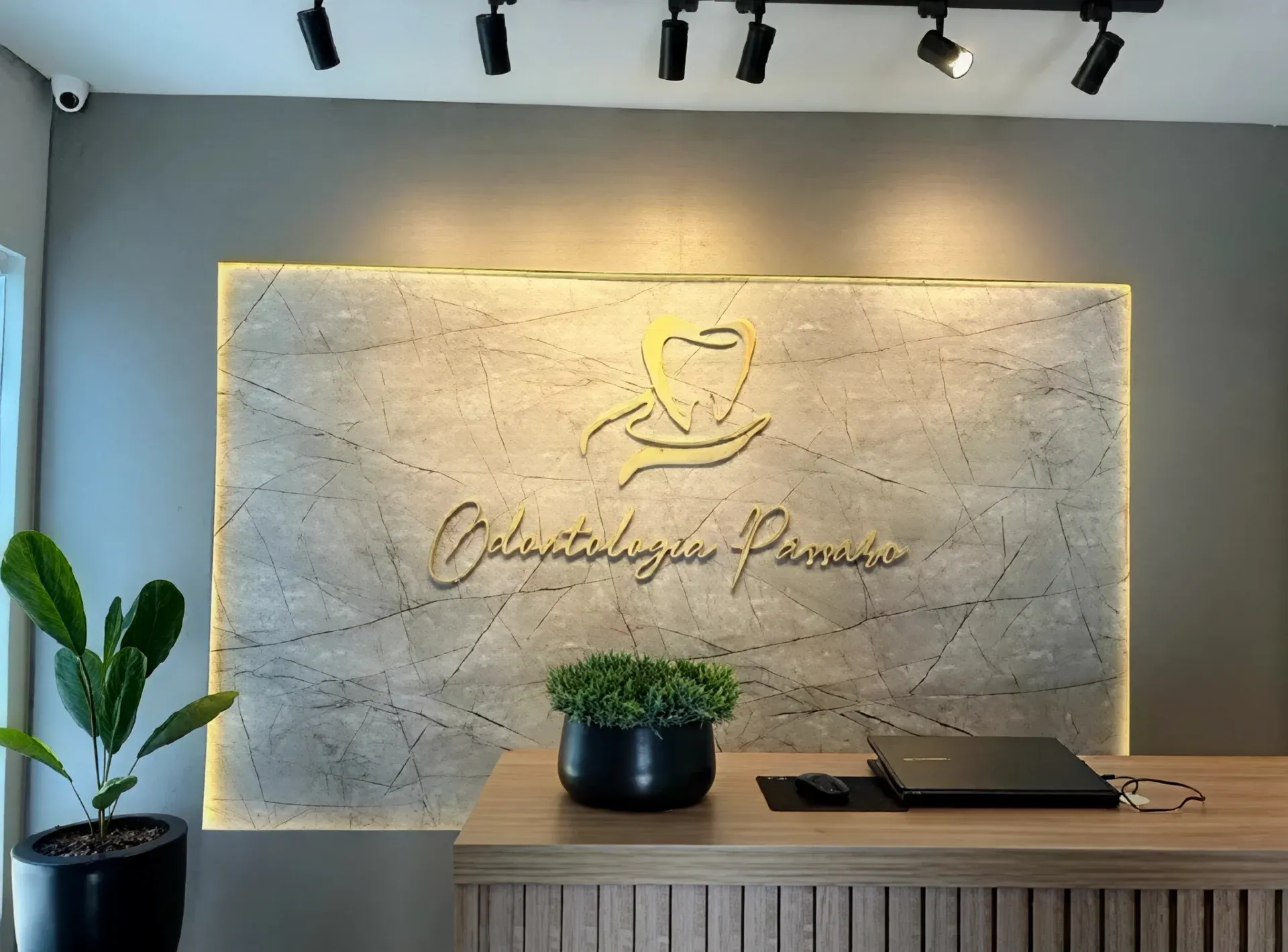 Recepção de consultório odontológico com balcão ripado e painel iluminado com logotipo