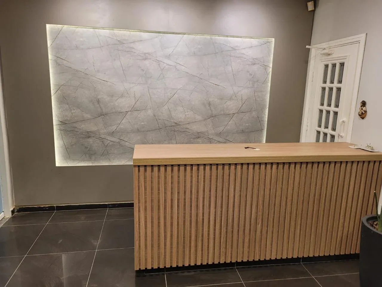 Visão ampla da recepção odontológica com balcão de madeira ripada e painel em LED