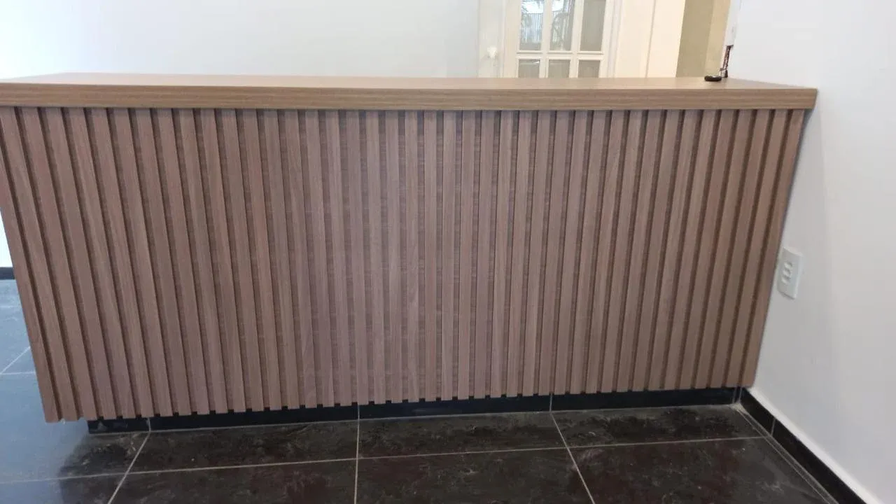 Detalhe do balcão ripado em madeira clara para recepção de clínica odontológica